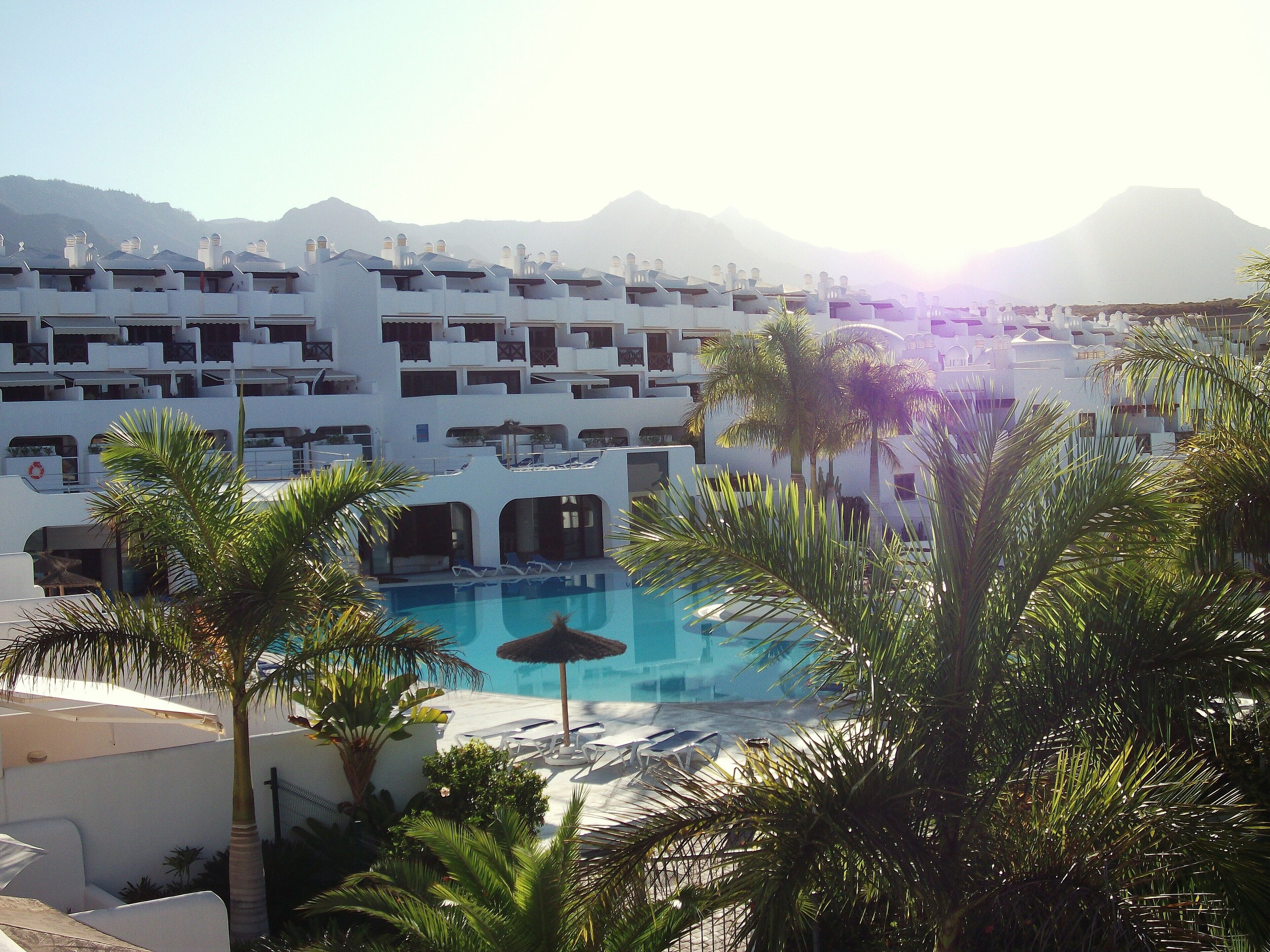 A resort with a pool surrounded by palm trees and white buildings.