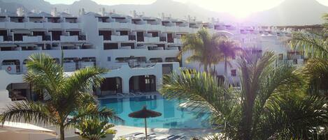 Un resort con piscina rodeada de palmeras y edificios blancos.