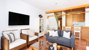 Un salon comprenant un canapé, deux fauteuils, une table basse et un téléviseur à écran plat fixé au mur.