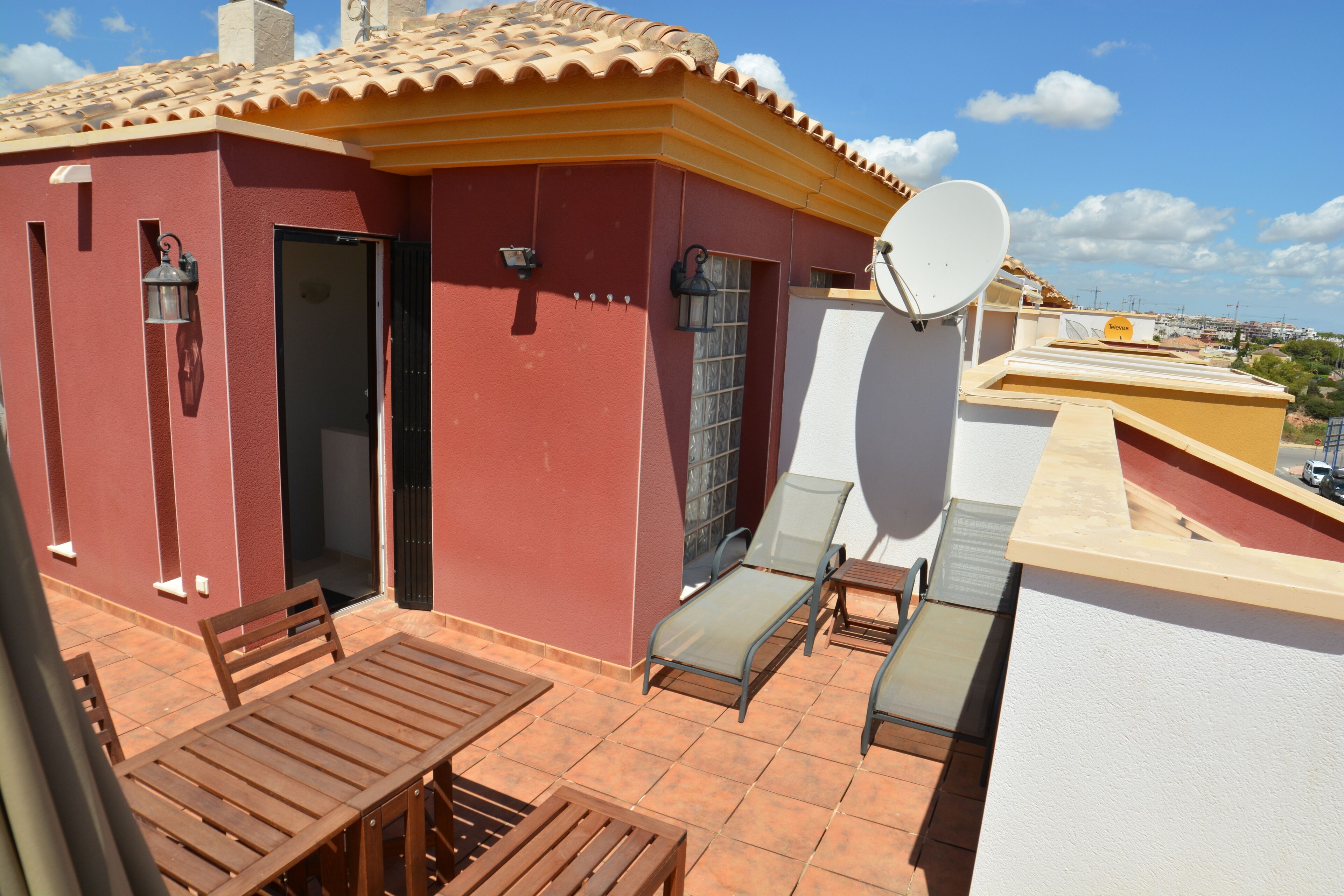 A red building with a tiled roof, a satellite dish, and a patio with wooden furniture.