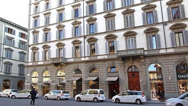 Ein mehrgeschossiges Gebäude im klassischen Stil, mit einer symmetrischen Fassade und gleichmäßig angeordneten Fenstern und Rundbogenportalen.