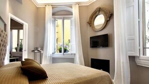 Ein Schlafzimmer mit Bett, Fernseher, einem Fenster mit Vorhängen und einem Spiegel an der Wand.