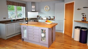 A kitchen with a central island, wooden countertop, and a built-in sink. There are cabinets with drawers and a window above the sink. - Exceptional House In Superb Location in NTS Conservation Area, Stunning Sea View (Kyle of Lochalsh)