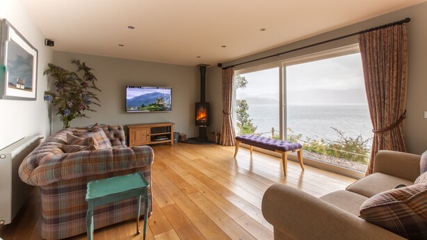 A living room with a large window, a television, a fireplace, and a sofa. - Exceptional House In Superb Location in NTS Conservation Area, Stunning Sea View (Kyle of Lochalsh)