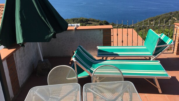 Una terraza con dos sillones reclinables a rayas verdes y una mesa, con vista al mar.