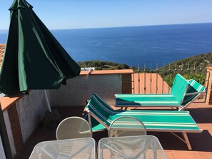 A terrace with two green-striped lounge chairs and a table, overlooking a coastal view. - VIGNA MARIA Holiday House l'Arancio (Zanca)