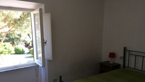Un dormitorio con cama, mesita de noche, ventana y vistas al exterior.