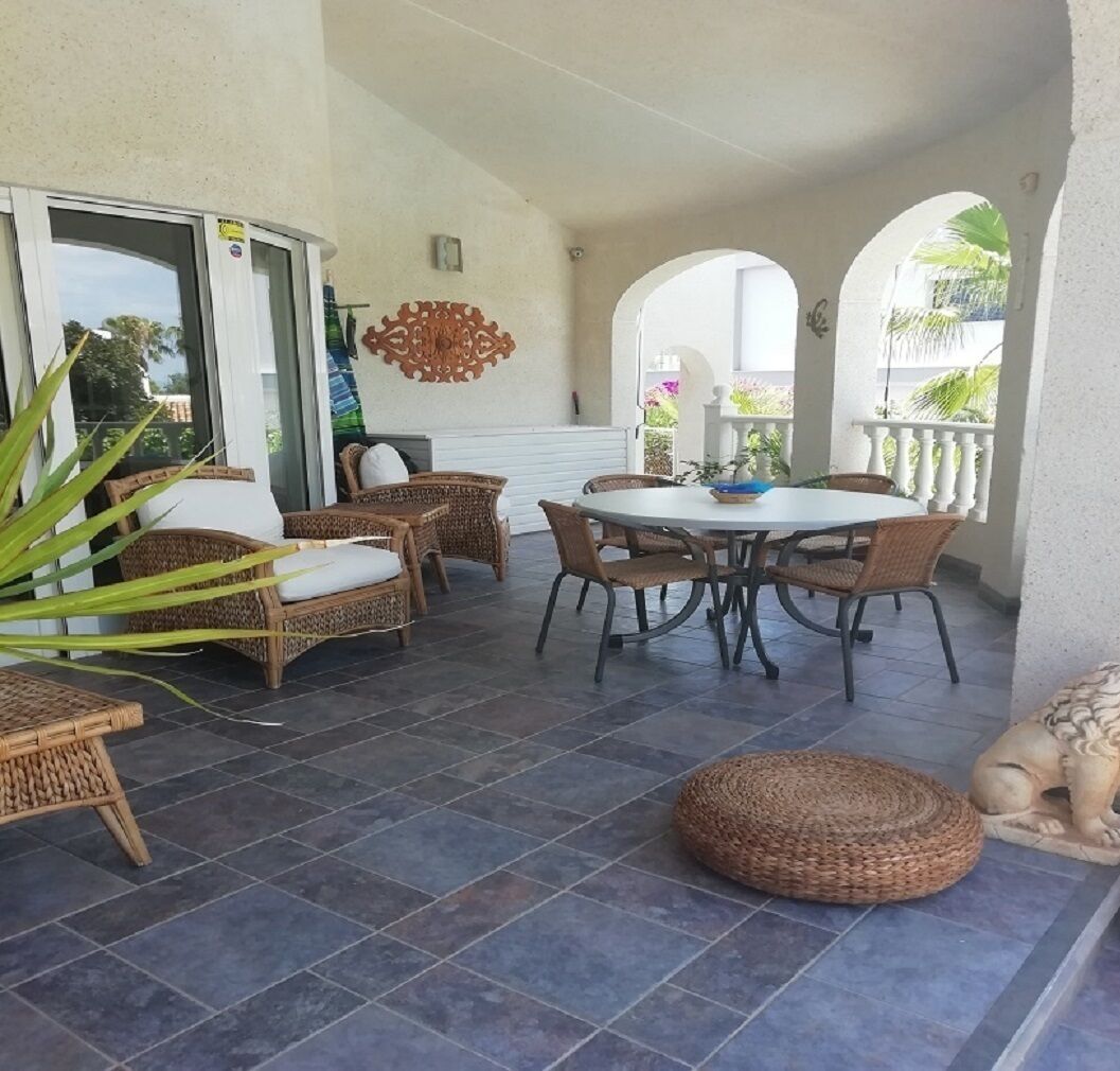 Un patio couvert aménagé avec des meubles en osier, une table ronde et un élément décoratif mural.