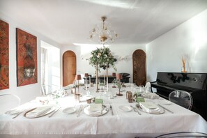 A dining room with a white table set for a meal, a chandelier, and a piano in the background.