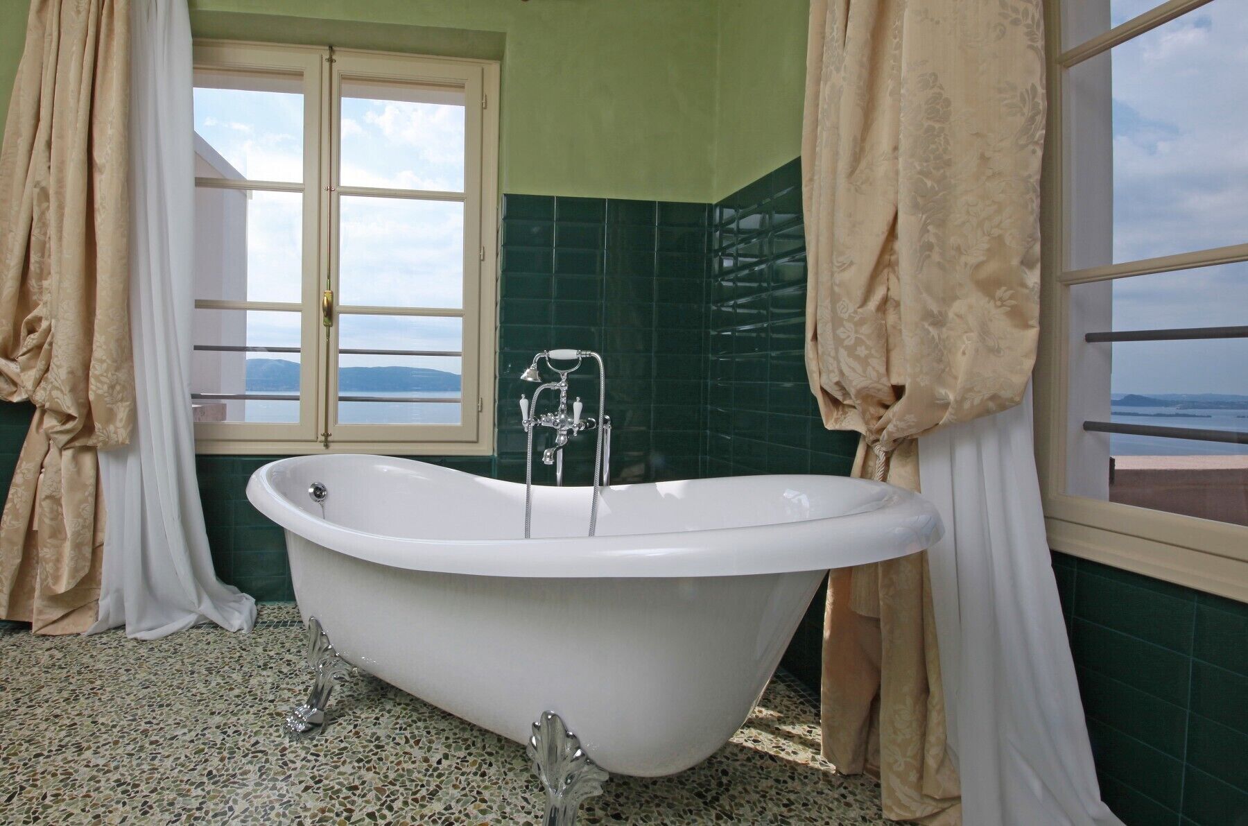 Une salle de bain avec une baignoire sur pieds, une fenêtre avec des rideaux et une vue sur la mer.