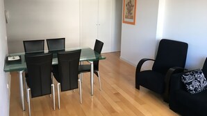 A modern dining area with a glass table and black chairs, a wooden floor, and a framed picture on the wall. - LisbonMeetU - Flat in Parque das Nações | T1 (Sacavém)