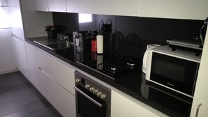 A modern kitchen with white cabinets, a black countertop, a built-in oven, a microwave, and a coffee maker. - LisbonMeetU - Flat in Parque das Nações | T1 (Sacavém)