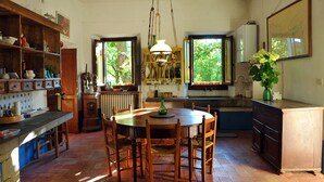 A kitchen with a round wooden table, wooden chairs, a hanging light fixture, and a window with a view of greenery. - An 800 villa in the Tuscan countryside - a quiet place - pool - culture (Londa)