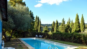 A rectangular swimming pool with a clear blue water surface, surrounded by a grassy area with a brick pathway leading to it. There are two white plastic chairs placed near the pool. - An 800 villa in the Tuscan countryside - a quiet place - pool - culture (Londa)