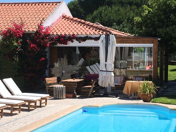 A poolside area with lounge chairs, a covered seating area with a table, and a clear blue pool.