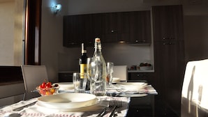 Une table à manger dressée avec des assiettes, des couverts et des verres, ainsi qu’une bouteille et un saladier de fruits posés sur la table.