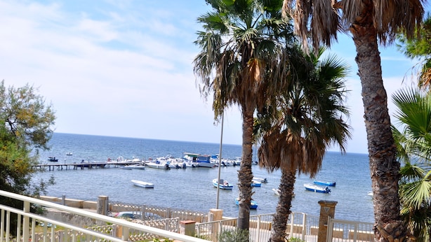 Un balcon avec une table dressée pour deux personnes, donnant sur une marina où l’on peut admirer des bateaux et des palmiers.
