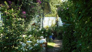 Ein schmaler Steinweg, gesäumt von üppigem Grün und blühenden Pflanzen, führt zu einem Hauseingang.