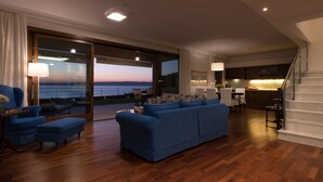 Uma sala de estar espaçosa com um amplo sofá azul, piso de madeira, área de jantar e cozinha.