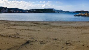 Uma praia com céu claro, águas calmas e colinas ao longe.