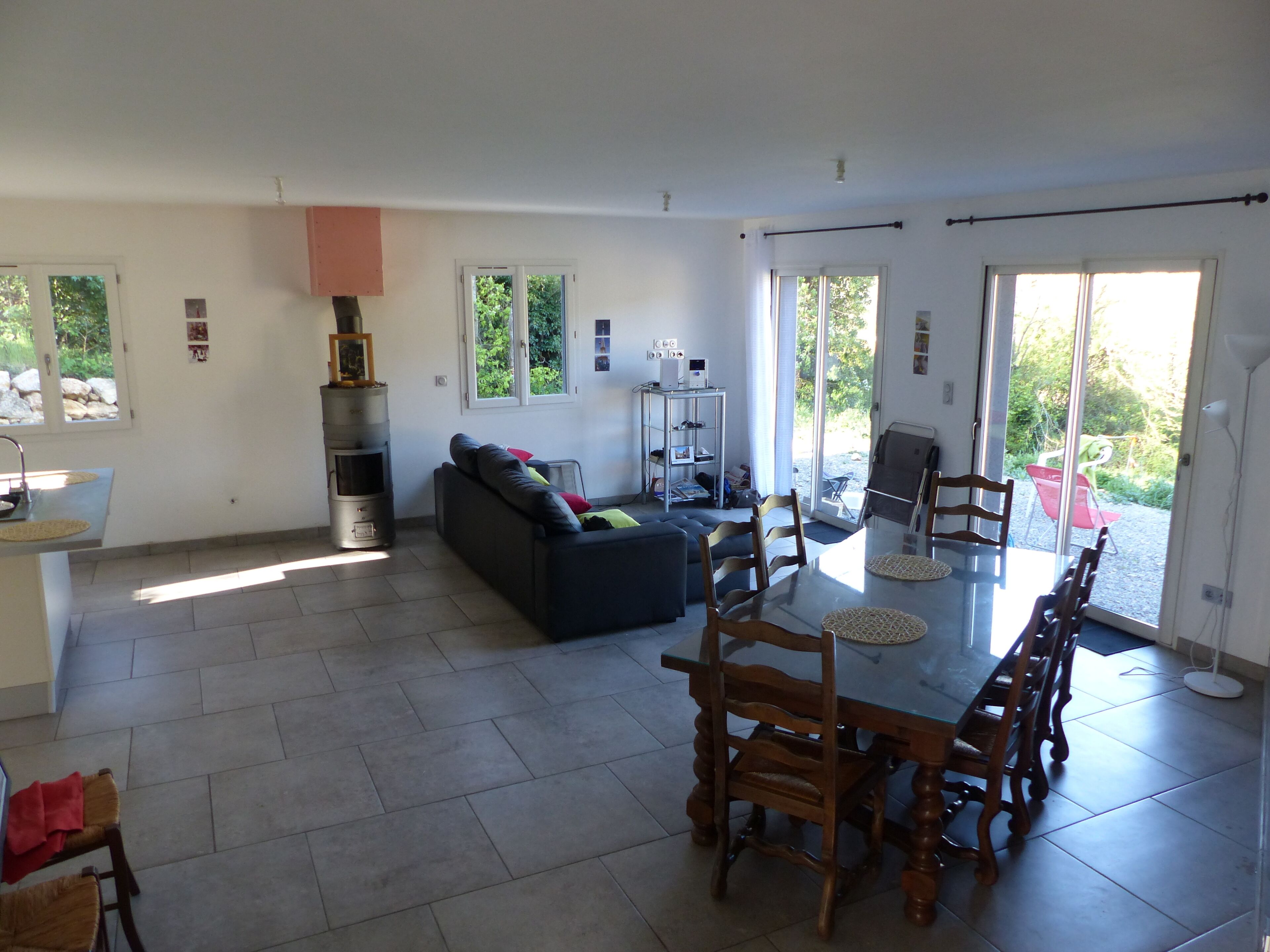 Een ruime woonkamer met een eettafel, houten stoelen, een bank en een open haard.