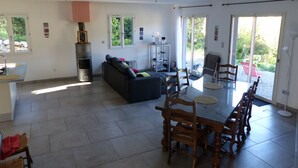 Een ruime woonkamer met een eettafel, houten stoelen, een bank en een open haard.