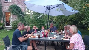 Eine Gruppe von Menschen speist im Freien an einem Tisch mit Sonnenschirm.