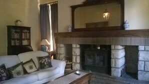 Ein Wohnzimmer mit Kamin aus Stein, einer Couch mit Kissen, einer Lampe und einem Bücherregal.