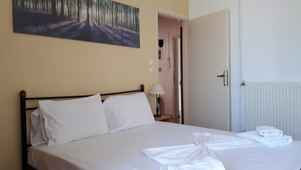 Uma cama bem arrumada com lençóis e toalhas brancas, uma luminária de cabeceira e um quadro com uma paisagem de floresta na parede.
