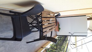 Um pátio externo com mesa e cadeiras de madeira, uma parede branca e um portão de metal.