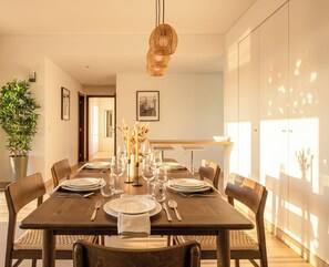 A dining area with a wooden table set for four, surrounded by chairs, with a hanging light fixture above.