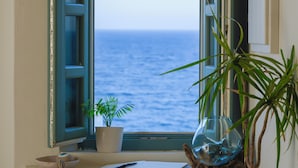 Una stanza con una finestra vista mare, una piccola pianta e una ciotola sul davanzale.