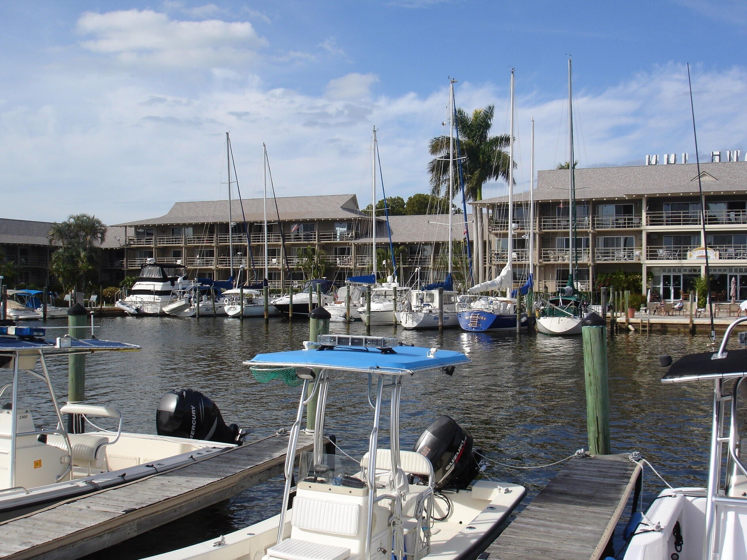 A marina with docked boats, a building with multiple balconies, and a clear sky.