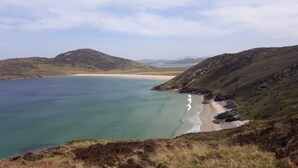 Paisatge costaner amb una platja, aigües clares i turons al voltant.