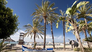 A beach scene with palm trees, a boat labeled "CHIRINGUITO - PEPE'S BAR", and a lifeguard tower. - Frontline Penthouse in quiet apartment block Marbella with stunning views  (Marbella)