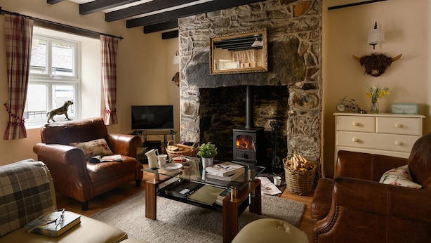 A cozy living room with a stone fireplace, leather sofas, a glass coffee table, and a television. - Tan Y Graig, Rhyd-Ddu, Snowdonia (Rhyd-Ddu)