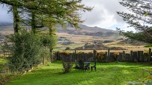A grassy outdoor area with a rustic fence, a small garden, and a metal table with chairs. - Tan Y Graig, Rhyd-Ddu, Snowdonia (Rhyd-Ddu)