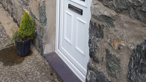 A stone building with a white door, a small window, and a potted plant. - Tan Y Graig, Rhyd-Ddu, Snowdonia (Rhyd-Ddu)