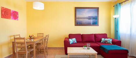 Una sala de estar con un sofá rojo, una mesa de comedor de madera, sillas y un cuadro en la pared.