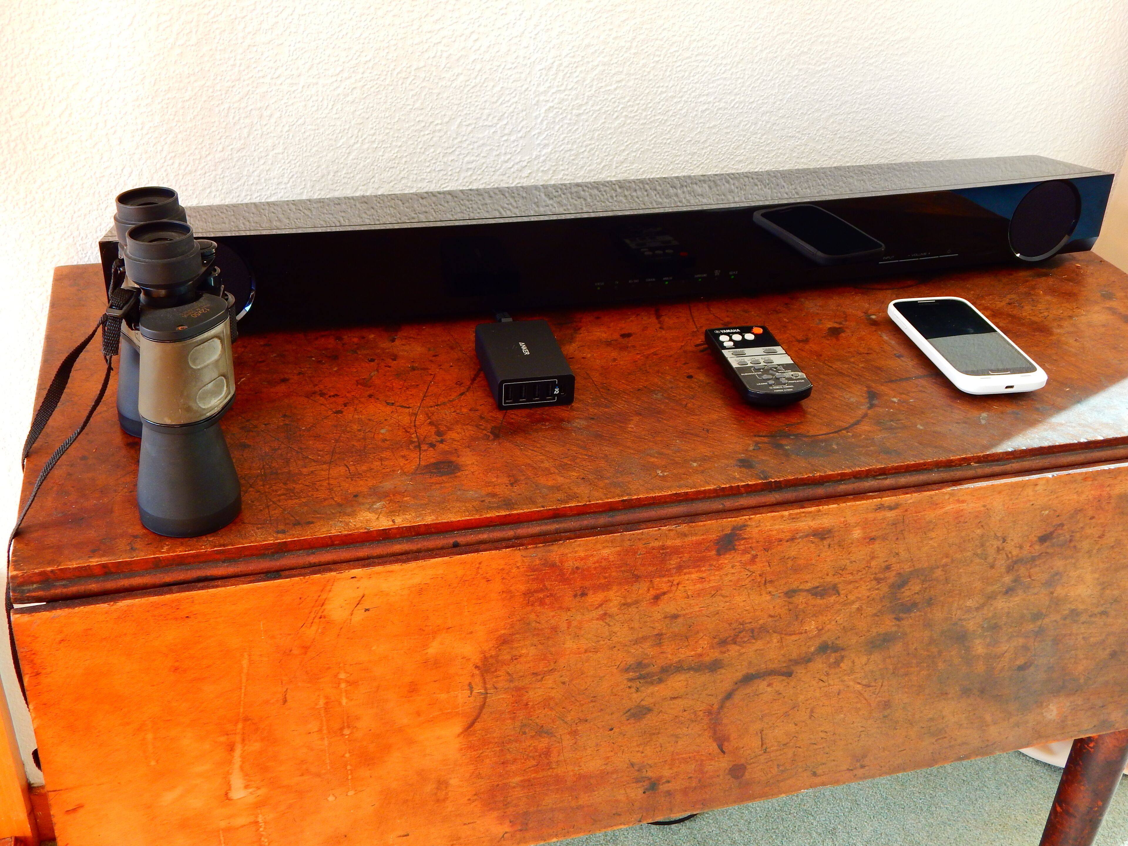 A wooden table with a telescope, a power bank, a remote control, and a smartphone.