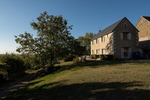 A stone building with a sloped roof, a large tree in front, and a clear sky. - La Maison – Spacious Loire Cottage with Heated Pool near Chinon & Azay le Rideau (Avon-Les-Roches)