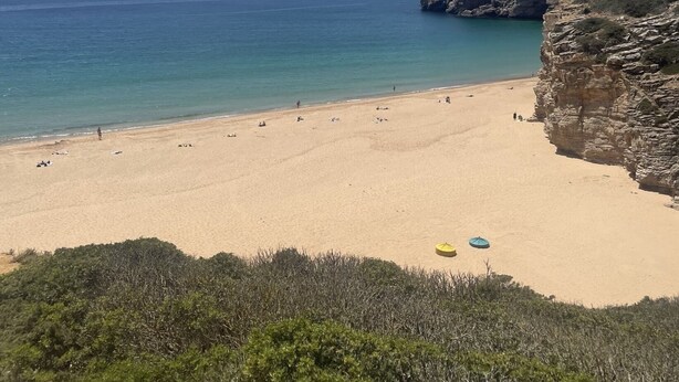 Une plage avec une eau d’un bleu limpide, un rivage sablonneux et des falaises rocheuses.