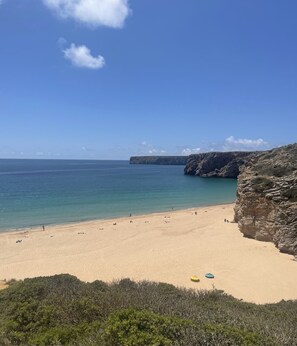 A beach with clear blue water, sandy shore, and rocky cliffs.