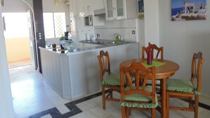 Una cocina moderna con armarios blancos, una isla central y una zona de comedor con sillas y mesa de madera.