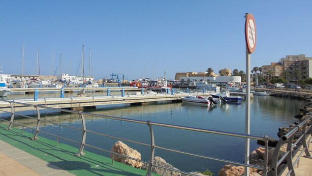 Marina con barcos amarrados, cielo despejado y un letrero que prohíbe bañarse.