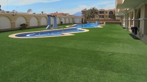 Zona de piscina con césped artificial, una fuente y un edificio con ventanas arqueadas.
