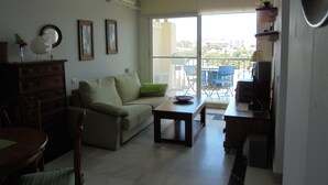 Una sala de estar con sofá, una mesa de centro y un mueble para la televisión. Hay un balcón con vistas a la ciudad.