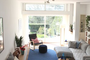 A bright living room with a large sliding glass door leading to a garden, a comfortable sofa, a rocking chair, and a bookshelf. - Spacious villa with private pool Rome 20 minutes away overlooking national park (Formello)