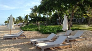 A beach with lounge chairs and umbrellas, palm trees, and a building in the background. - Lovely apartment near Flic en Flac beach, the sunniest west coast of Mauritius.  (Les Orchidees)