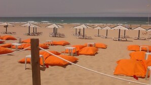 A beach with rows of white lounge chairs and orange cushions, some with umbrellas.